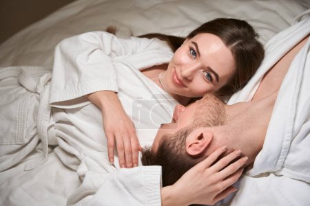 Téléchargez les photos : Souriant jeune femme heureuse couchée à côté de son partenaire romantique dans un lit confortable - en image libre de droit