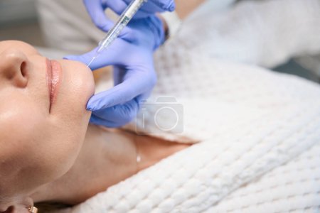 Foto de Primer plano de manos cosmetólogas haciendo inyección para suavizar las arrugas en la cara de la mujer madura en el salón de belleza - Imagen libre de derechos