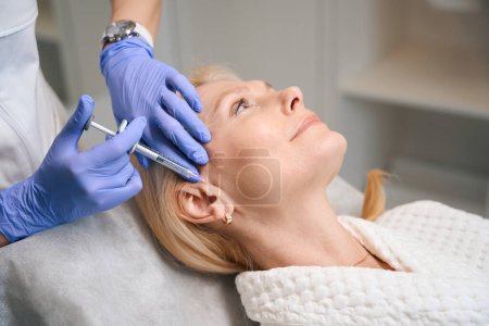 Photo for Cosmetologist hands performing rejuvenating injection on mature ladys ear area in beauty salon - Royalty Free Image