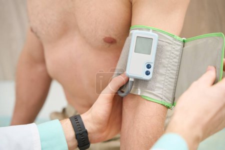 Photo for Doctor putting tonometer on arm of male for health examination in the hospital - Royalty Free Image