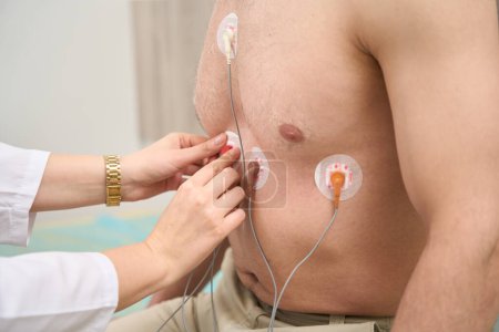 Foto de Enfermera poniendo sensores en macho para electrocardiografía del sistema cardiovascular en la clínica - Imagen libre de derechos