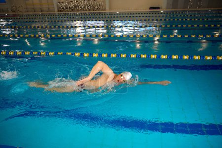 Foto de Hombre adulto con gorra blanca y gafas que practican deportes nadando en la piscina - Imagen libre de derechos