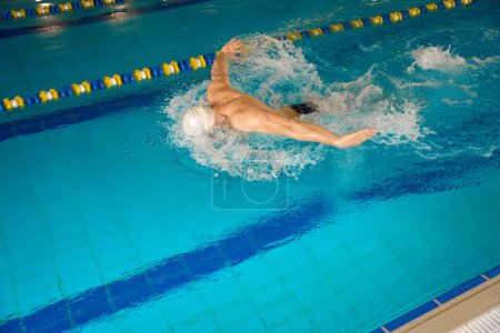 Photo for Sportsman in white cap engaged in sports swimming, man warming up before training in the pool - Royalty Free Image