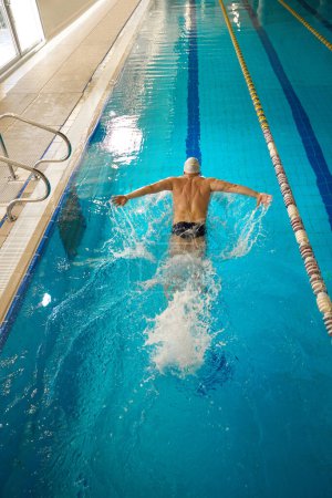 Téléchargez les photos : Nageur professionnel en casquette et lunettes blanches engagées dans des exercices sportifs de style papillon dans la piscine - en image libre de droit
