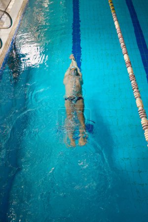 Foto de Hombre adulto en gorra blanca nadando en estilo delfín, atleta se dedica al entrenamiento muscular en el agua - Imagen libre de derechos