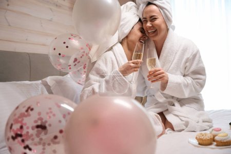 Téléchargez les photos : Heureux deux femmes cliquetis verres avec du vin mousseux et rire dans la chambre d'hôtel de luxe - en image libre de droit