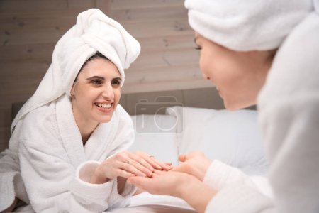 Téléchargez les photos : Jeunes femmes profitant du plaisir après les procédures de spa ensemble dans un hôtel de luxe, portant des serviettes sur les têtes et des peignoirs - en image libre de droit