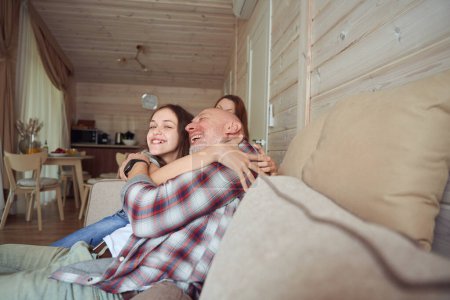 Téléchargez les photos : Souriant jeune fille heureuse assise sur le canapé embrassant son père heureux en présence de la mère - en image libre de droit