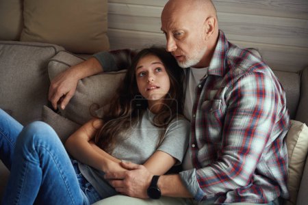 Téléchargez les photos : Adolescente préoccupée couchée sur le canapé dans la chambre tout en regardant son père cher sérieux - en image libre de droit