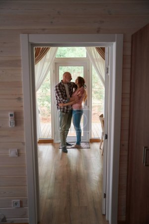 Foto de Retrato de tamaño completo de los cónyuges amorosos abrazándose mientras están de pie en la habitación en la puerta principal de vidrio - Imagen libre de derechos