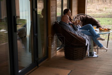 Photo for Dreamy woman with cup of herbal beverage sitting on lap of pensive man on veranda - Royalty Free Image