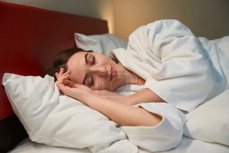 Téléchargez les photos : Sereine jeune femme couchée avec les yeux fermés dans un lit confortable pendant le sommeil - en image libre de droit