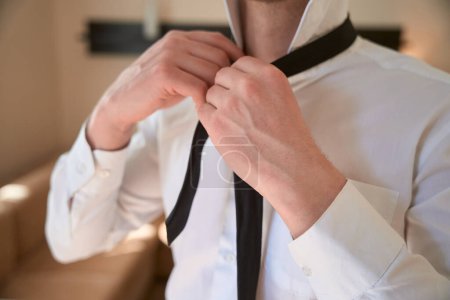 Foto de Foto de cerca del joven macho atándose la corbata en la habitación del motel - Imagen libre de derechos
