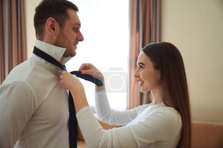 Photo for Happy woman looking at young male and helping to dress in the hotel room - Royalty Free Image