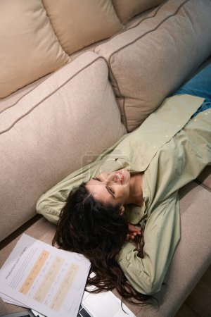 Foto de Relajada mujer joven freelancer acostado en cómodo sofá tomando un descanso en el papeleo, trabajo remoto portátil - Imagen libre de derechos