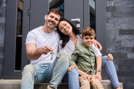 Foto de Familia joven se sienta con las llaves en la mano delante de la puerta de una nueva casa - Imagen libre de derechos