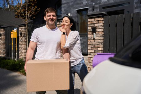 Téléchargez les photos : Femme étreignant son mari pendant qu'il tient la boîte de déménagement - en image libre de droit