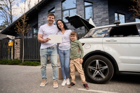 Téléchargez les photos : Un câlin familial se tient devant une maison et une voiture - en image libre de droit