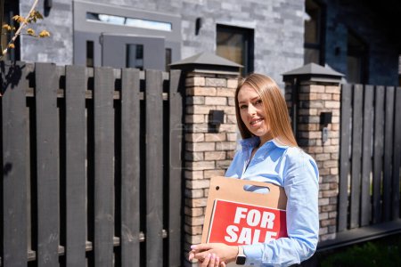 Téléchargez les photos : Caucasienne jeune femme agent immobilier sur le fond de la maison regarde droit dans la caméra souriant - en image libre de droit