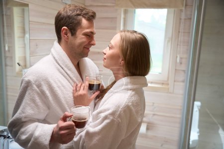 Foto de Hombre y mujer mirándose con café en las manos en el baño - Imagen libre de derechos