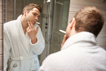 Téléchargez les photos : Jeune homme regardant dans le miroir avec une brosse à dents dans la bouche - en image libre de droit