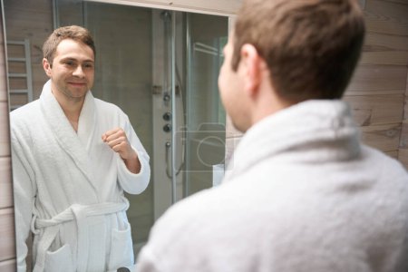 Foto de Hombre sonriente mirándose en el espejo mientras está de pie en el baño - Imagen libre de derechos