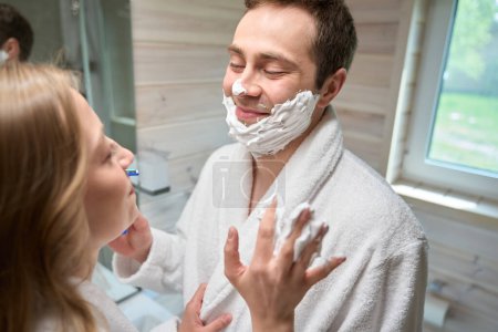 Photo for Man and a woman are standing in the bathroom looking at each other, a man with foam on his face - Royalty Free Image