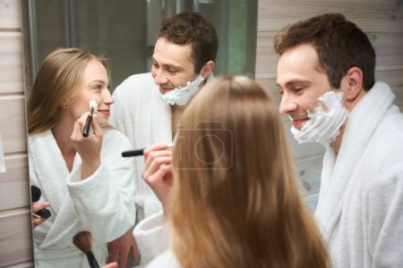 Photo for Woman putting on makeup standing in the bathroom Smiling man looking at woman - Royalty Free Image
