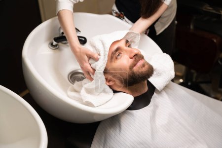 Friseurinnen waschen den Kopf einer Kundin an einem speziellen Waschbecken, Männer in einem schützenden Umhang