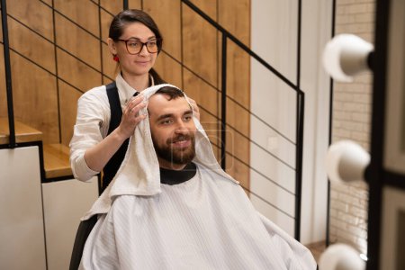 Téléchargez les photos : Barber sèche les cheveux du client avec une serviette douce, le mâle est situé dans la chaise de coiffure - en image libre de droit