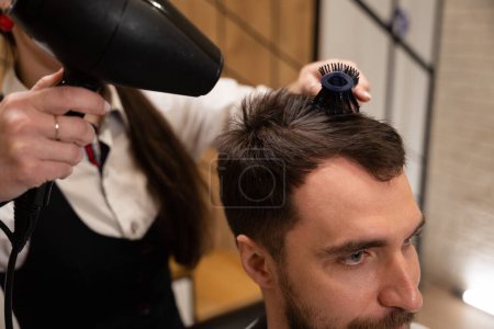 Téléchargez les photos : Artisanat faisant coiffure à un client, elle utilise un sèche-cheveux et une brosse à coiffer - en image libre de droit