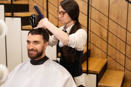 Photo for Satisfied man sitting in a barber chair ,the craftswoman does his hair styling - Royalty Free Image