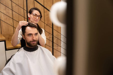 Foto de Artesana trabaja con un cliente en una barbería moderna, un hombre con una capa protectora - Imagen libre de derechos