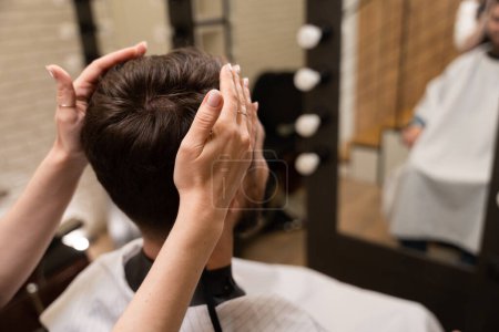Foto de Artesana en una peluquería hace un peinado masculino, el cliente se encuentra en frente del espejo - Imagen libre de derechos
