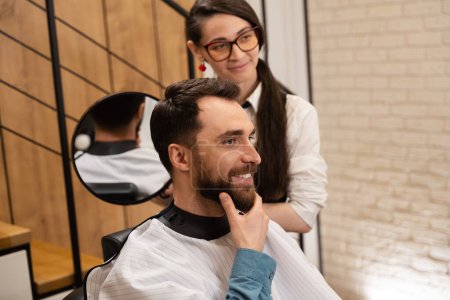 Téléchargez les photos : Femme coiffeuse montre sa coiffure du dos au client dans le miroir, le client sourit - en image libre de droit