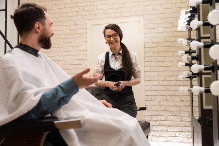Photo for Client and the master communicate cheerfully in the barbershop, indoors modern interior - Royalty Free Image