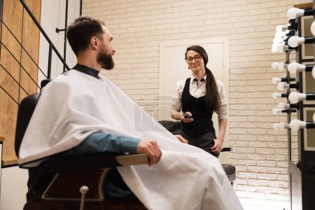 Téléchargez les photos : Le client barbu communique avec le maître dans le salon de coiffure, intérieur intérieur moderne - en image libre de droit