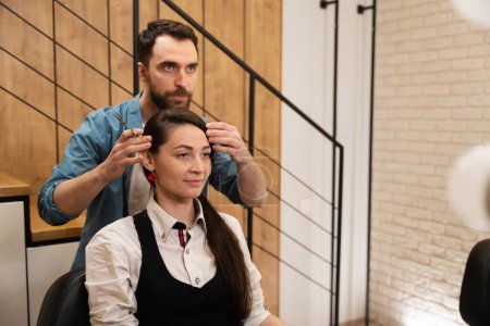 Téléchargez les photos : Homme barbu conseille une jeune femme dans un salon de coiffure, la femme est située dans une chaise confortable - en image libre de droit