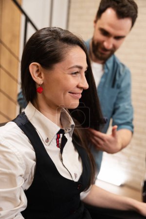 Téléchargez les photos : Maître peigne les cheveux d'une jeune femme avec une brosse coiffante, la femelle est située dans une chaise confortable - en image libre de droit