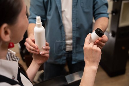 Photo for Male demonstrates jars of care products to a young woman, people are in a beauty salon - Royalty Free Image
