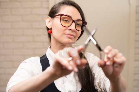 Photo for Female barber holding hairdressing scissors in her hands, a woman with glasses and a red earring - Royalty Free Image