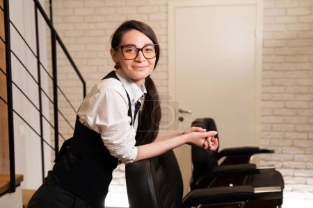 Téléchargez les photos : Femme avec des lunettes se tient à la chaise de coiffure, intérieur minimaliste intérieur - en image libre de droit