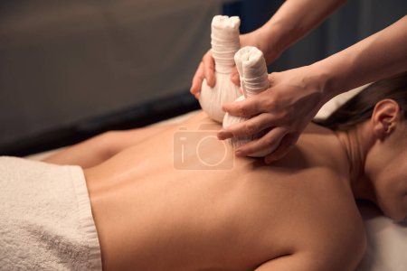 Photo for Cropped photo of massotherapist massaging female patient trapezius area with pair of hot herbal balls - Royalty Free Image