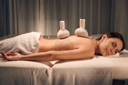 Photo for Calm spa customer lying on massage bed with pair of herbal balls on her back - Royalty Free Image