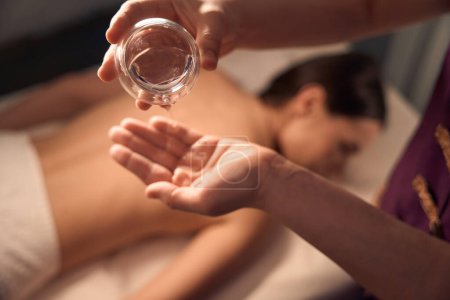 Photo for Cropped photo of spa therapist pouring oil from bowl on palm of her hand in presence of patient - Royalty Free Image