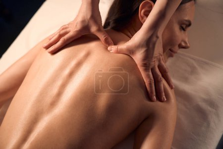 Téléchargez les photos : Masseuse mains pressant dans trapèze noeud musculaire sur le haut du dos du patient féminin - en image libre de droit
