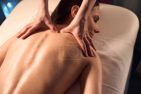 Foto de Mujer acostada propensa mientras masoterapeuta manos aplicando presión a trapecio punto de disparo - Imagen libre de derechos