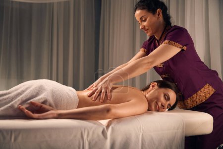 Photo for Woman lying prone with eyes closed while masseuse massaging her lumbar spine - Royalty Free Image
