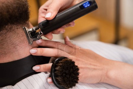 Téléchargez les photos : Femme barbier coupe une barbe mans, le maître utilise une tondeuse à barbe spéciale - en image libre de droit