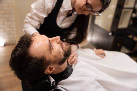 Téléchargez les photos : Homme dans un salon de coiffure se coupant la barbe, le maître utilise des outils spéciaux - en image libre de droit